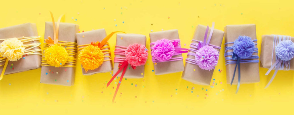 A bunch of colorfully gift wrapped boxed lined up on a bright yellow paper