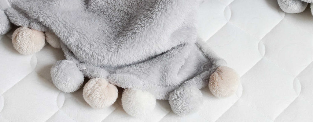 A close up of a light gray blanket with pom pom