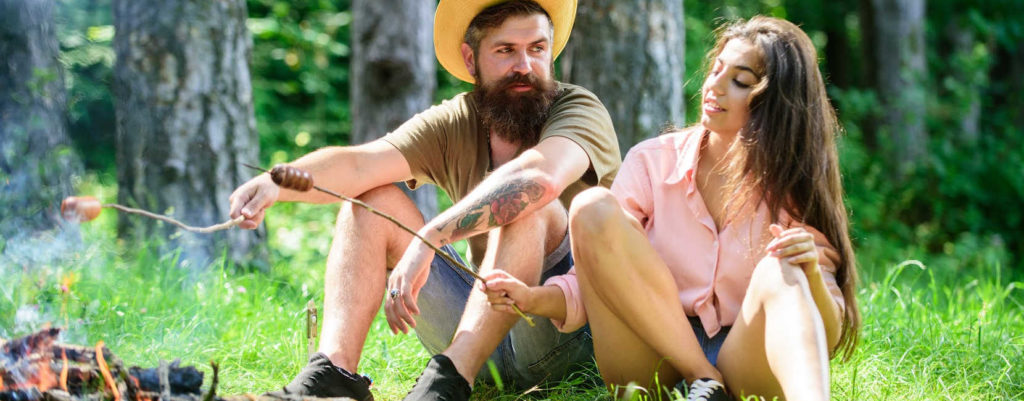 A couple sitting in the woods and grilling sausages in open fire