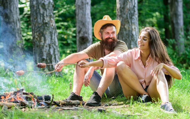 A couple sitting in the woods and grilling sausages in open fire