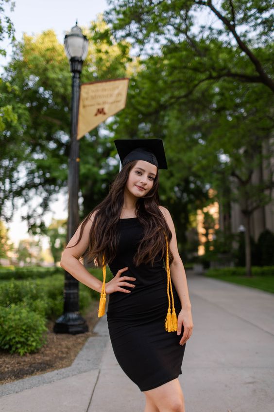 A young woman wearing a black dress with a black graduation cap.