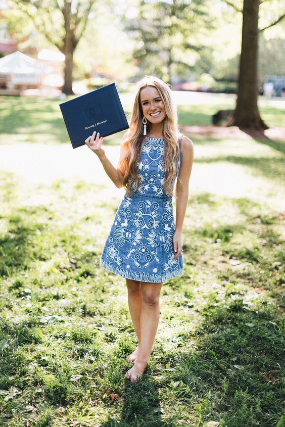 A woman wearing blue floral dress holding a diploma.