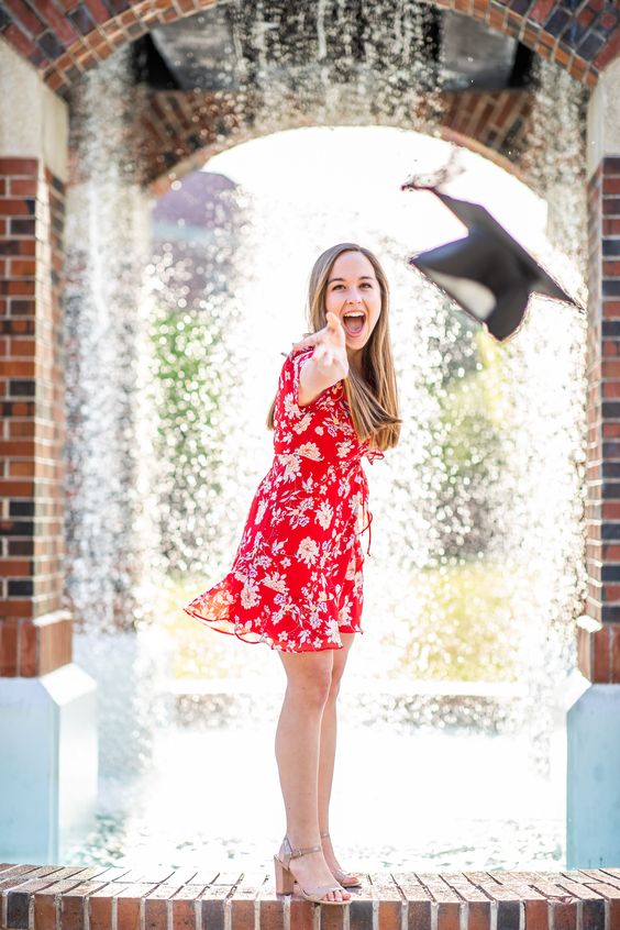 A young graduate wearing a red floral dress throw a cap.