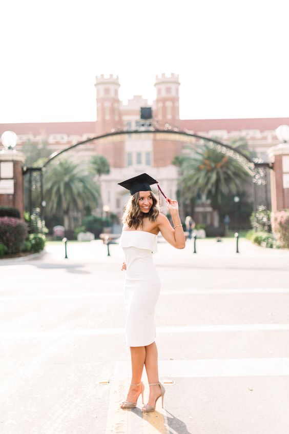 A young woman wearing a white dress and a black graduation cap.