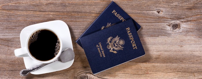 A couple of US passports and a cup of coffee on a wooden table.