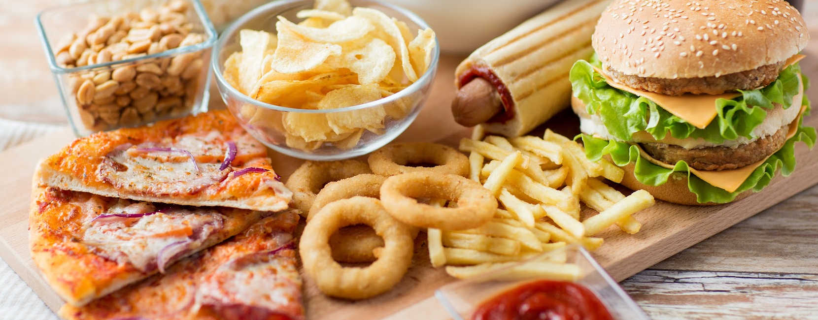 A bunch of fast foods on the table including pizza, burgers, hot dogs, and fries.
