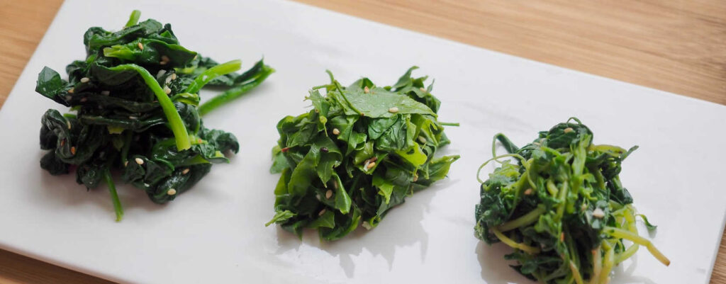 Three bunch of seasoned spinach on a glossy white plate.