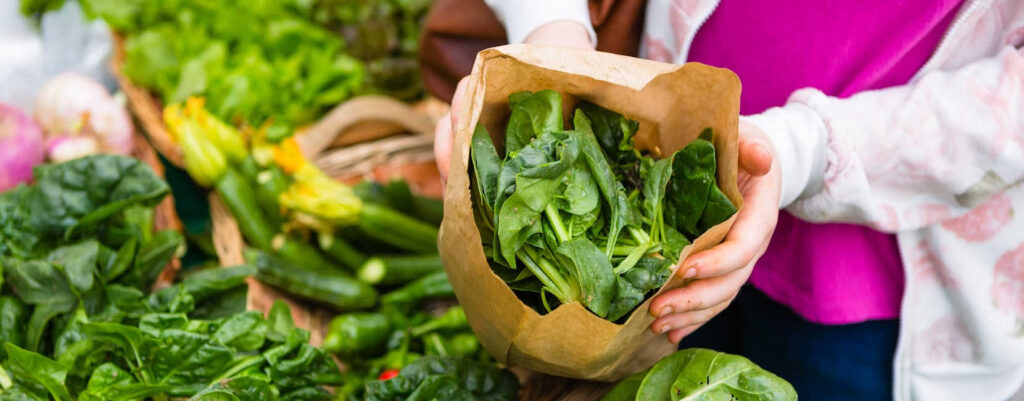 A woman holding a paper bag full of fresh spinach at the market.