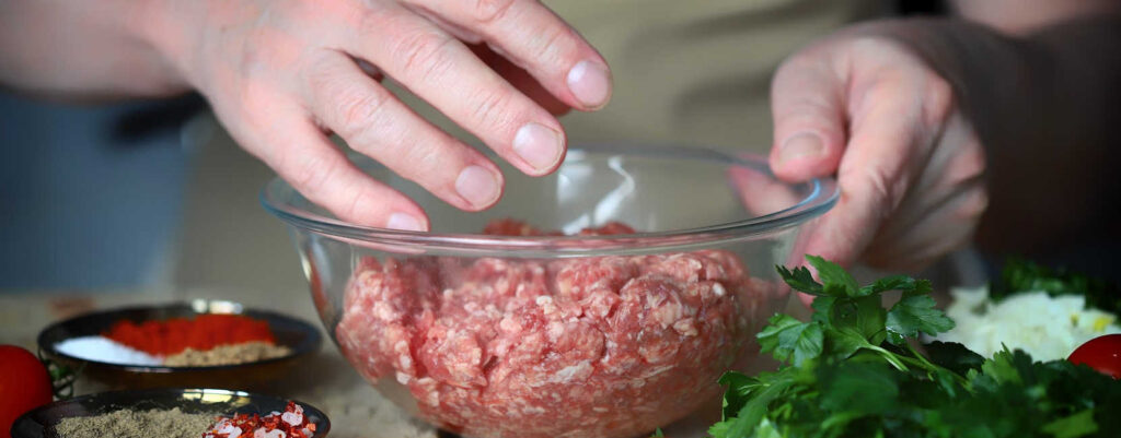 Mixing ground beef in a glass mixing bowl using hands.