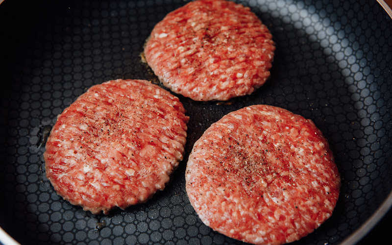 Three fresh ground burger patties on a pan.
