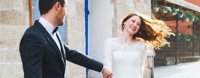 A bride has a big smile on her face as she's holding groom's hand.