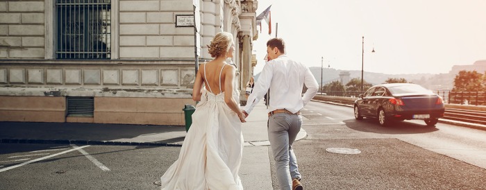 A bride and a groom holding hands and running towards a building.