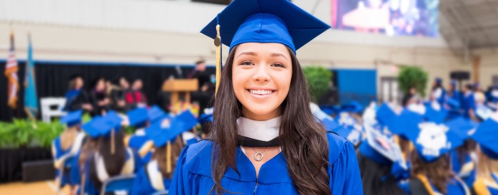 A young woman is wearing bright blue graduation regalia and smiling.