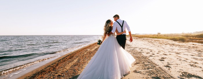 A bride and groom walking on the sandy beach.