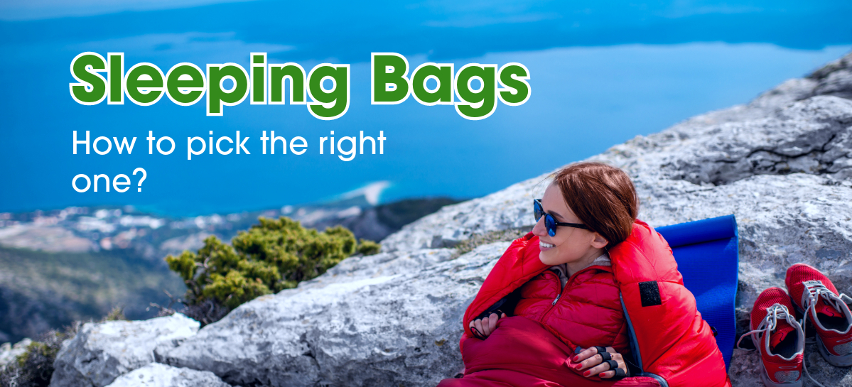 A woman in a red sleeping bag sitting on a rocky mountain top looking at the skyline.