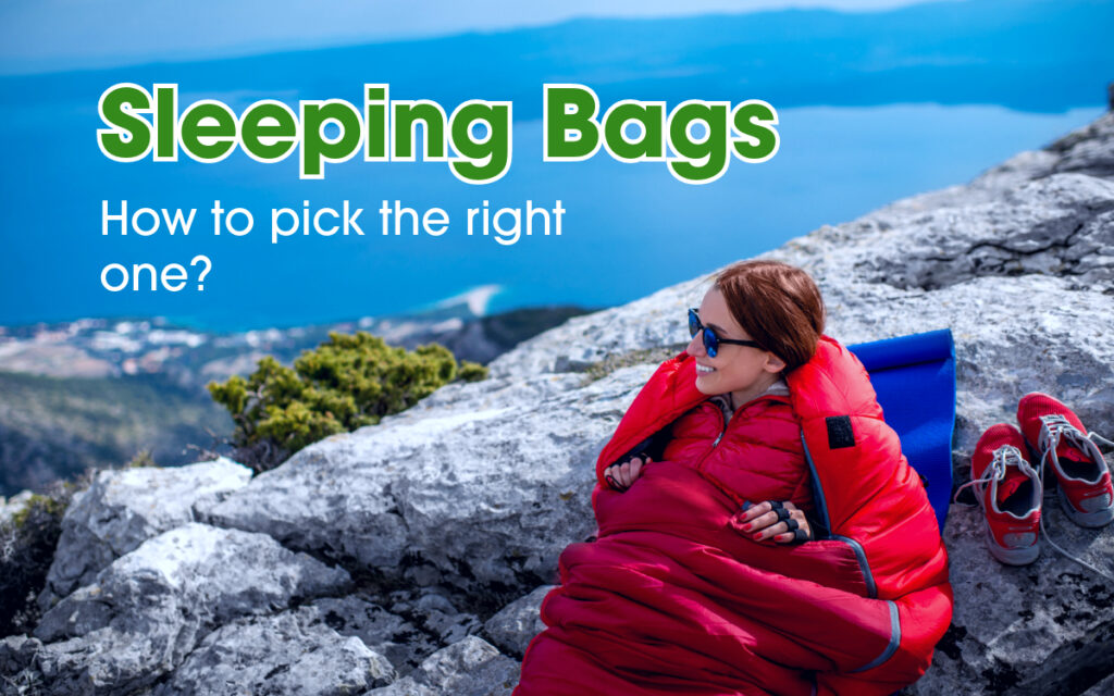 A woman in a red sleeping bag sitting on a rocky mountain top looking at the skyline.