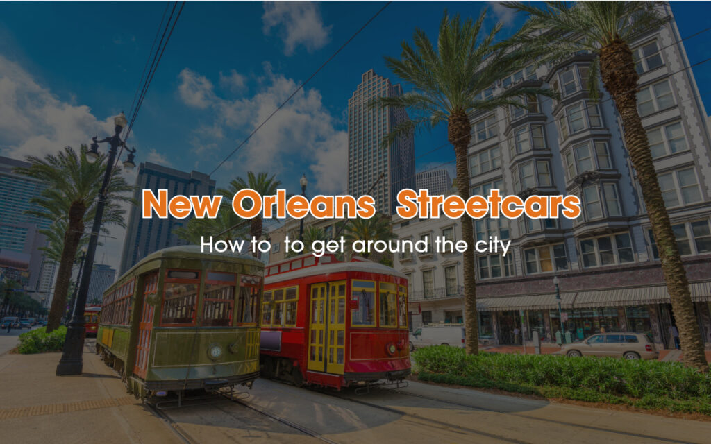 A couple of New Orleans' Streetcars are passing through the street between palm trees and tall buildings.
