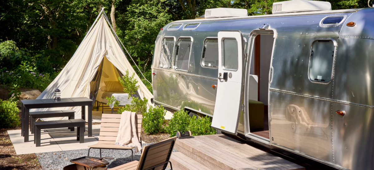 Airstream bus and tent in a camp ground.