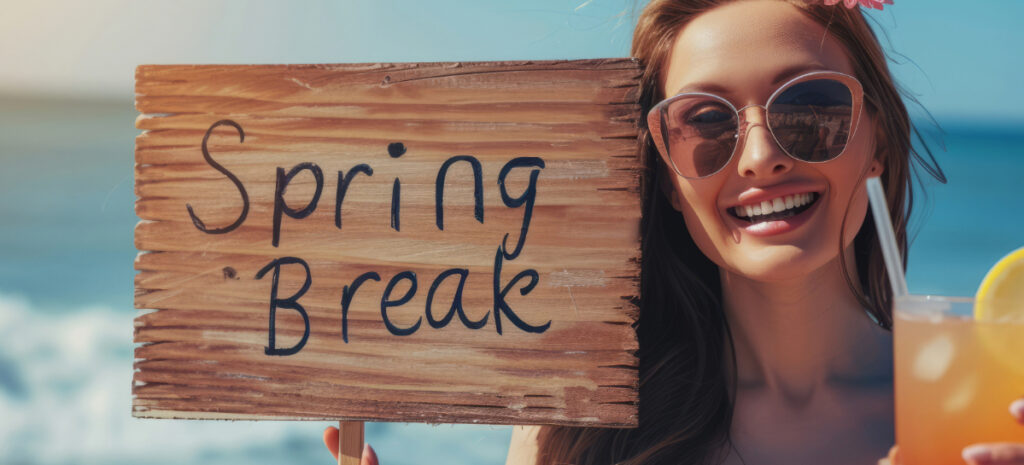 A woman wearing sunglasses holding a wooden sign that says Spring Break.