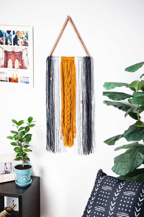 A yarn wall hanging on a white wall with photos and planters