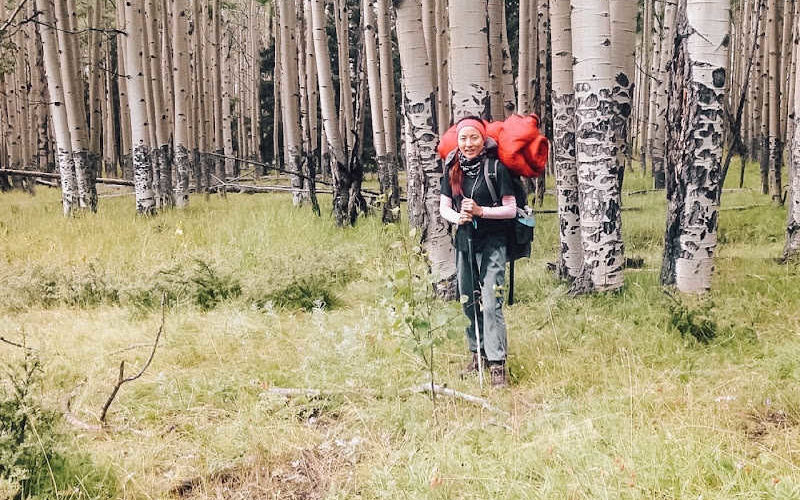 A woman hiker standing in front of a dense forest.