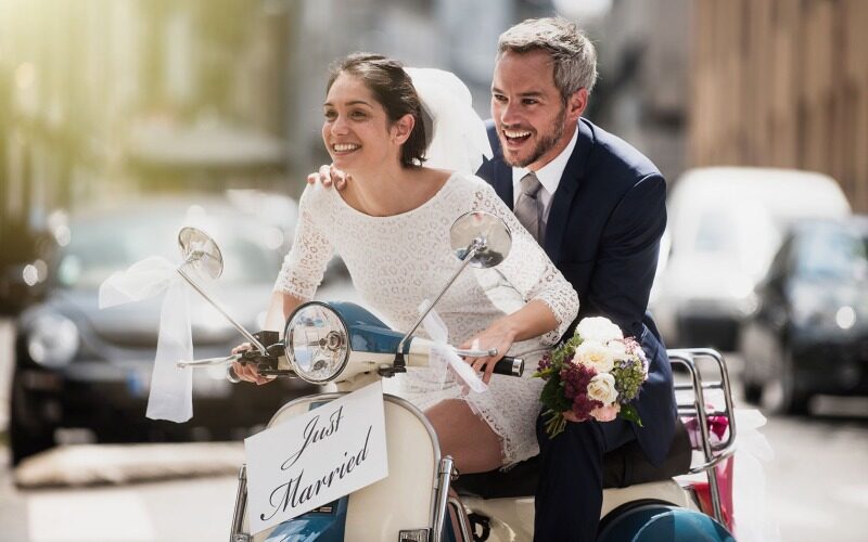 A newly weds riding a small bike with a sign that says, "Just Married."