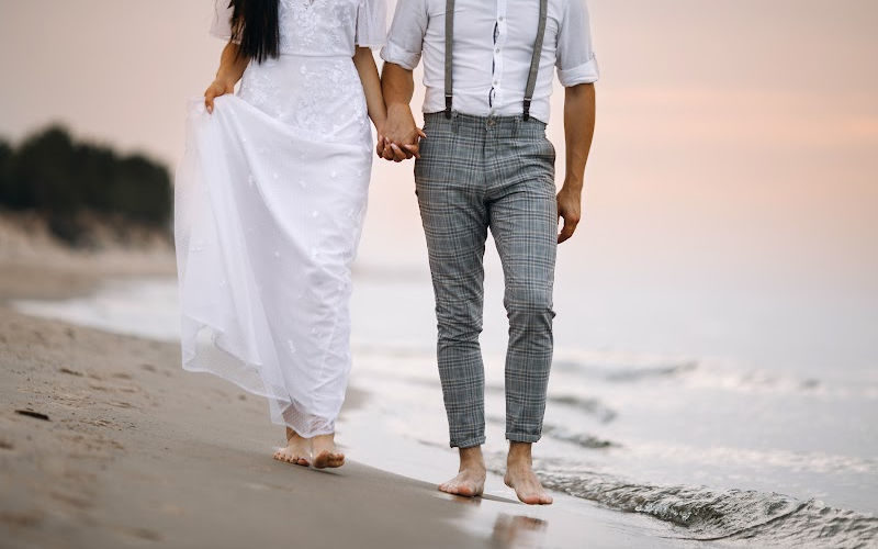 A newly weds holding hand and walking on the sandy beach.