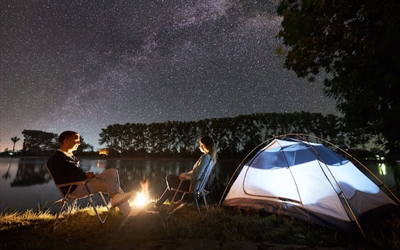 A couple of people sitting by the tent and campfire at night