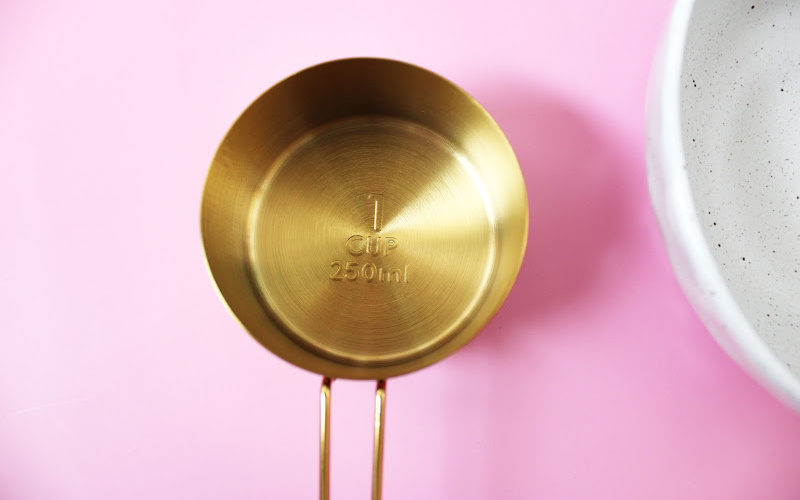 A gold plated measuring cup on pink background