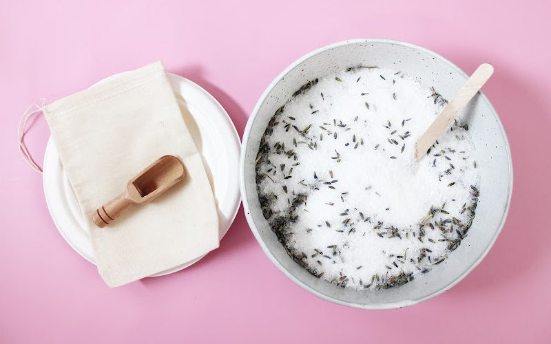 A bowl of lavender foot soak with bamboo scoop