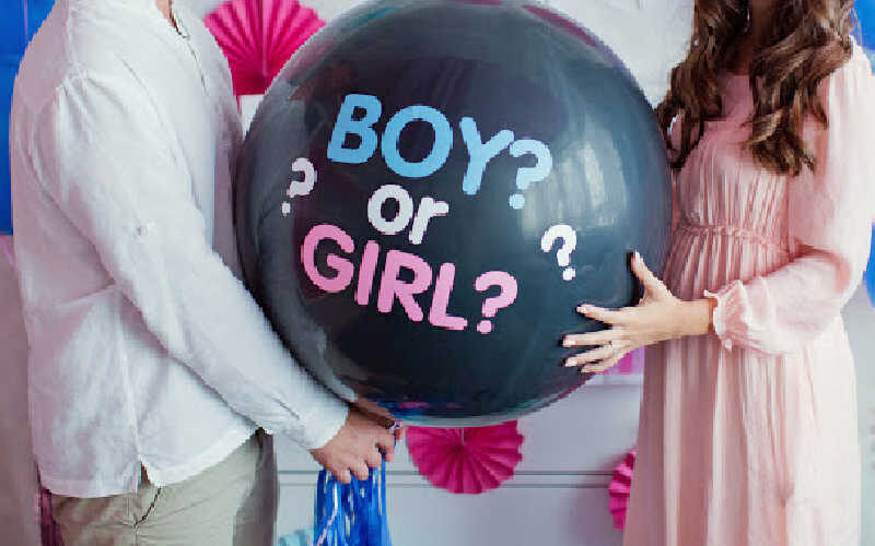 A couple holding a giant black balloon says Boy? or Girl?