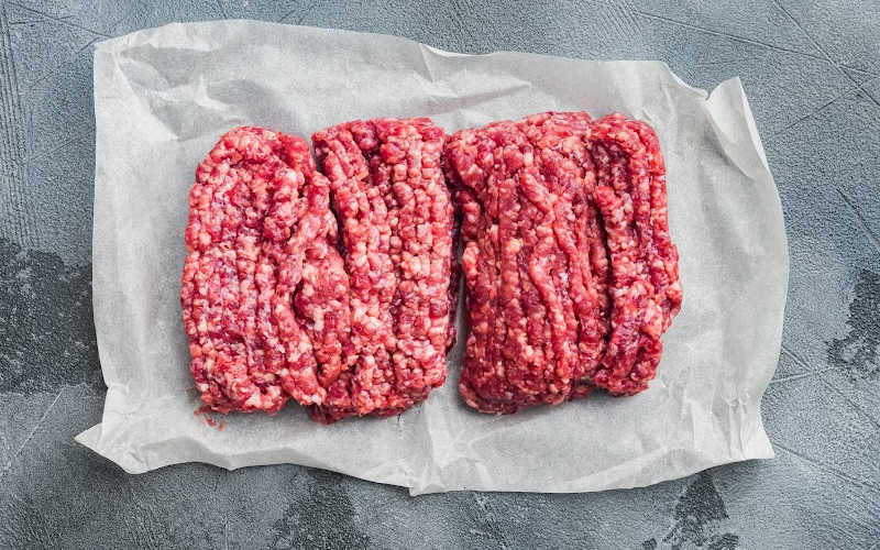 Two square chunks of fresh ground beef on a parchment paper.