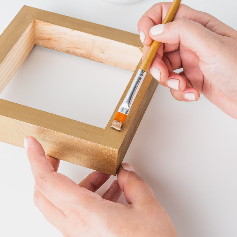 Someone applying gold paint to a wooden frame