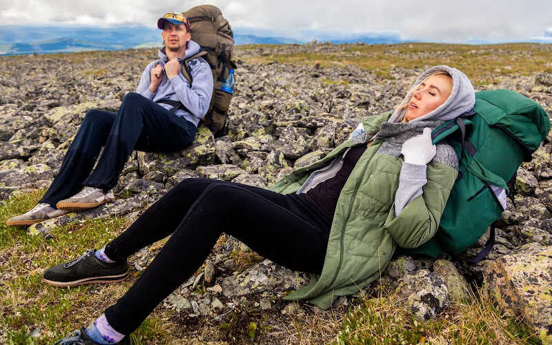 A couple of tired hikers laying on a rocky mountain with their heavy backpacks.