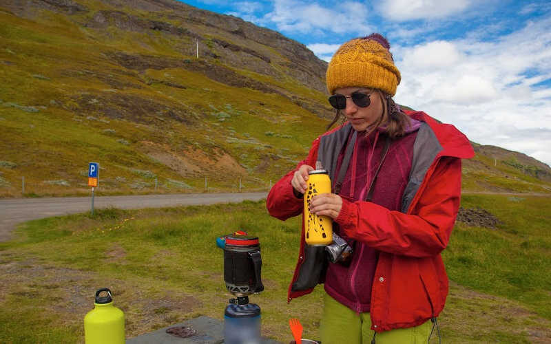 A hiker holding a yellow tumbler in the mountains.