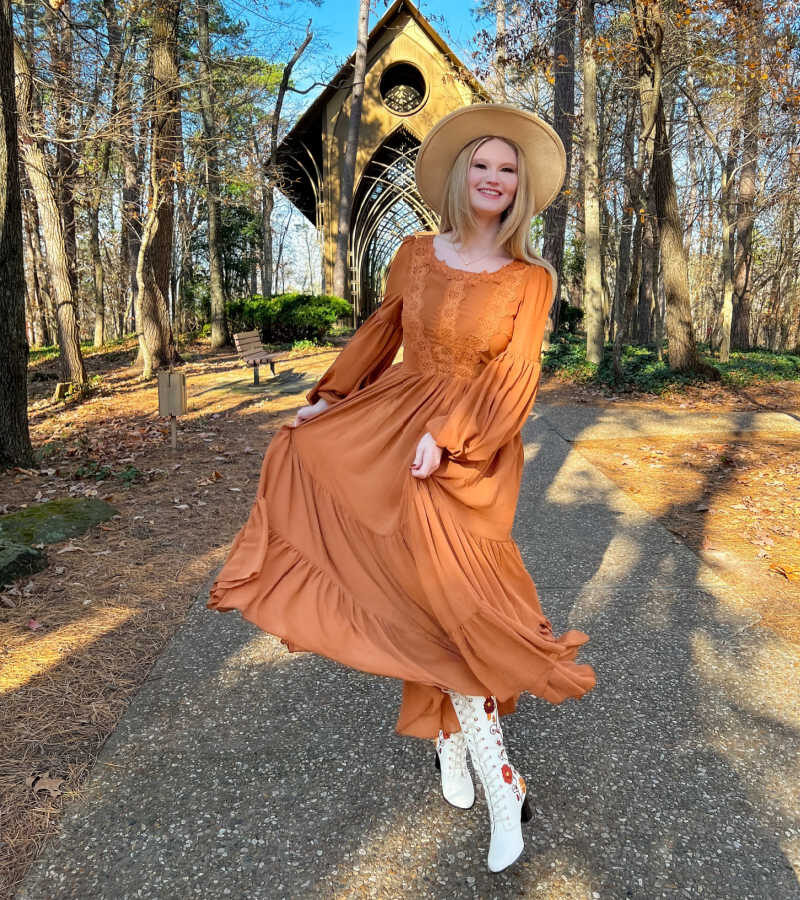 A woman wearing fall dress with hat and Western boots.