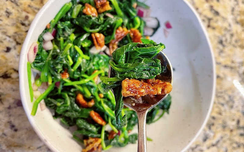 A bowl of seasoned spinach with candied walnuts.