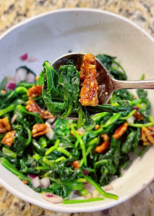 A bowl of seasoned spinach with candied walnuts.