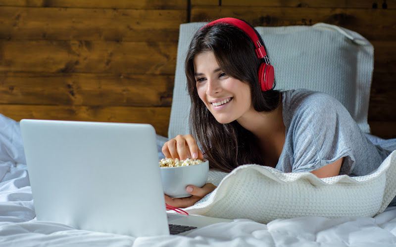 A woman is watching something on her laptop while holding a bowl of popcorn