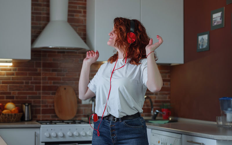 A woman wearing a read headphone and dancing in the kitchen