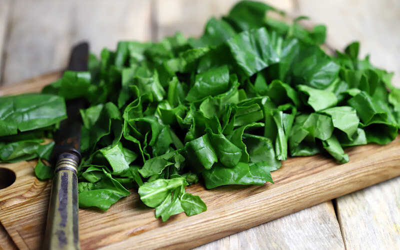 Freshly chopped spinach leaves on a bamboo cutting board with a antique knife.