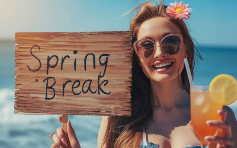 A woman wearing sunglasses holding a wooden sign that says Spring Break.