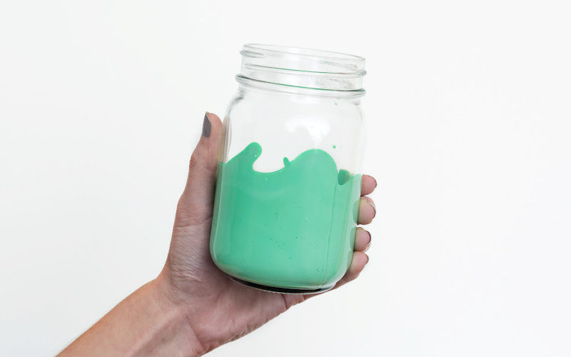 A hand holding a mason jar with bright green paint in it