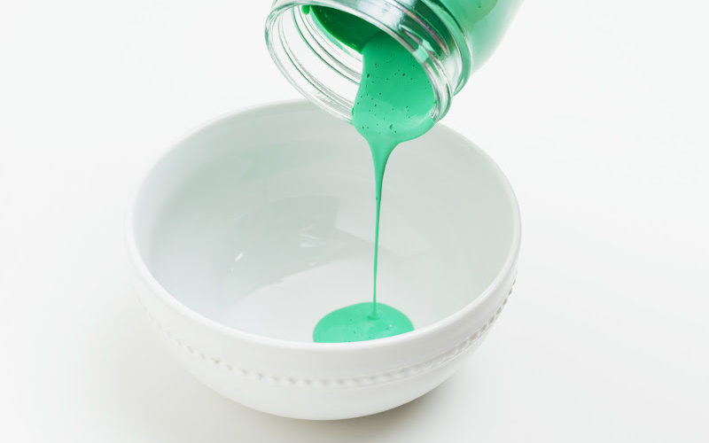 Pouring bright green paint into a white bowl