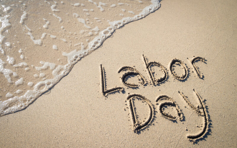 The letter Labor Day written on a sandy beach.