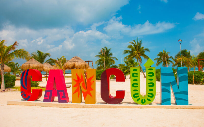 A colorful and large sign says Cancun on the beach.