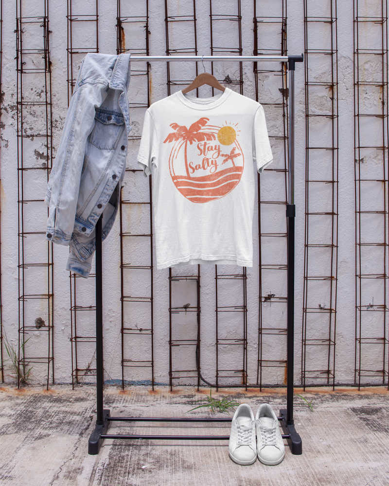 Stay Salty white graphic shirt hanging on a clothing rack on the street.