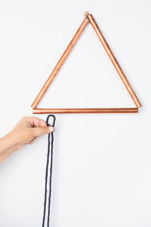 Someone holding up a yarn against a triangle metal rod